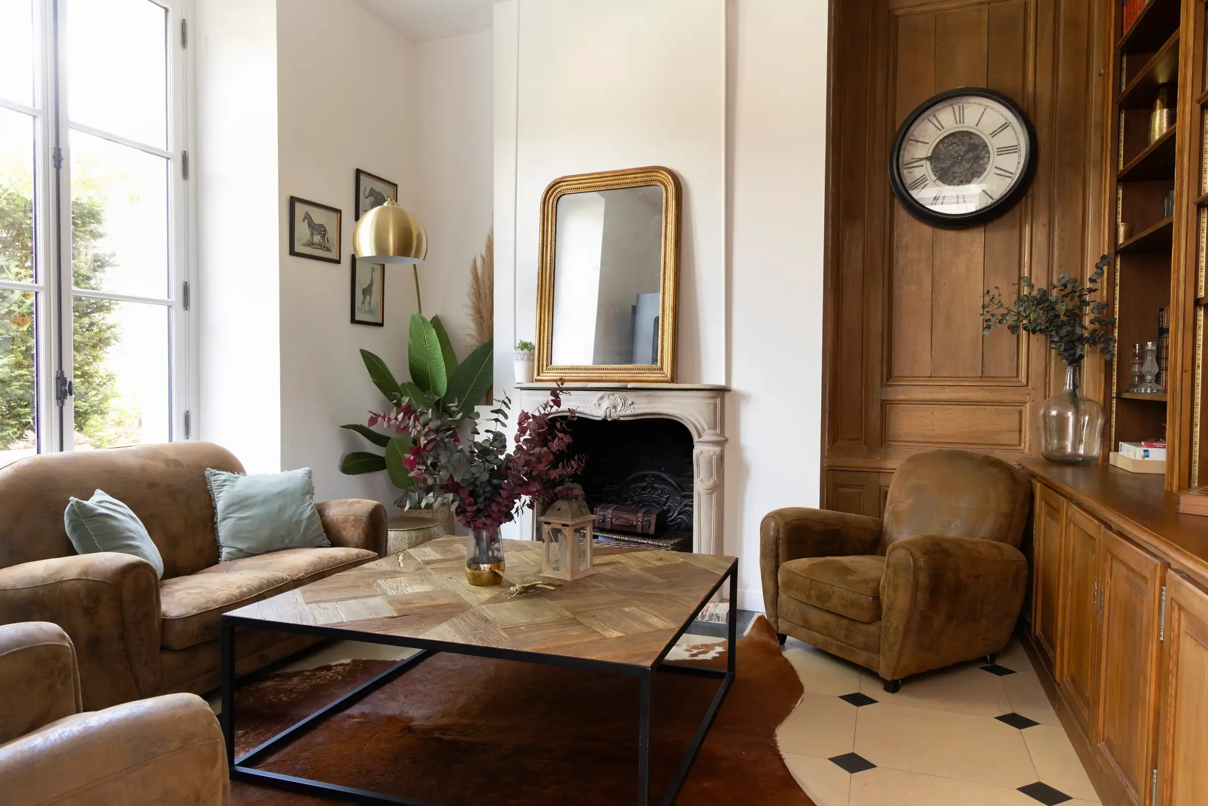 Salon avec canapé, fauteuils, table basse, cheminée, miroir, horloge et plantes décoratives