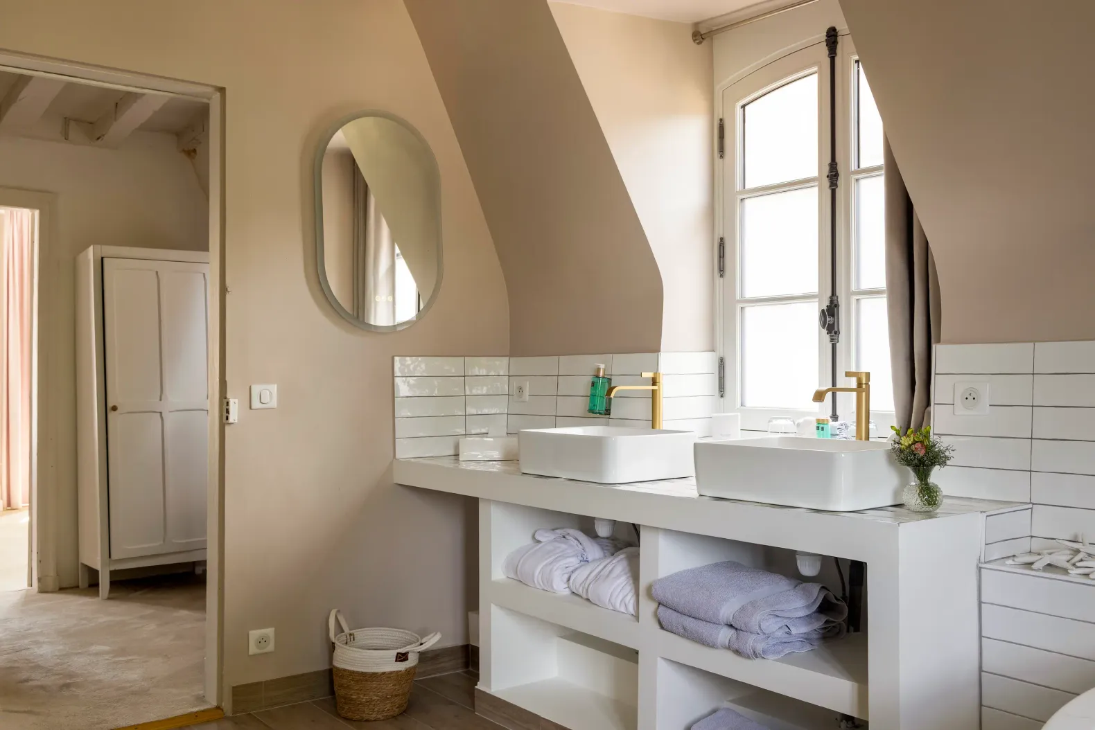 Salle de bain avec double vasque, miroir ovale, étagères de rangement et fenêtre avec rideaux