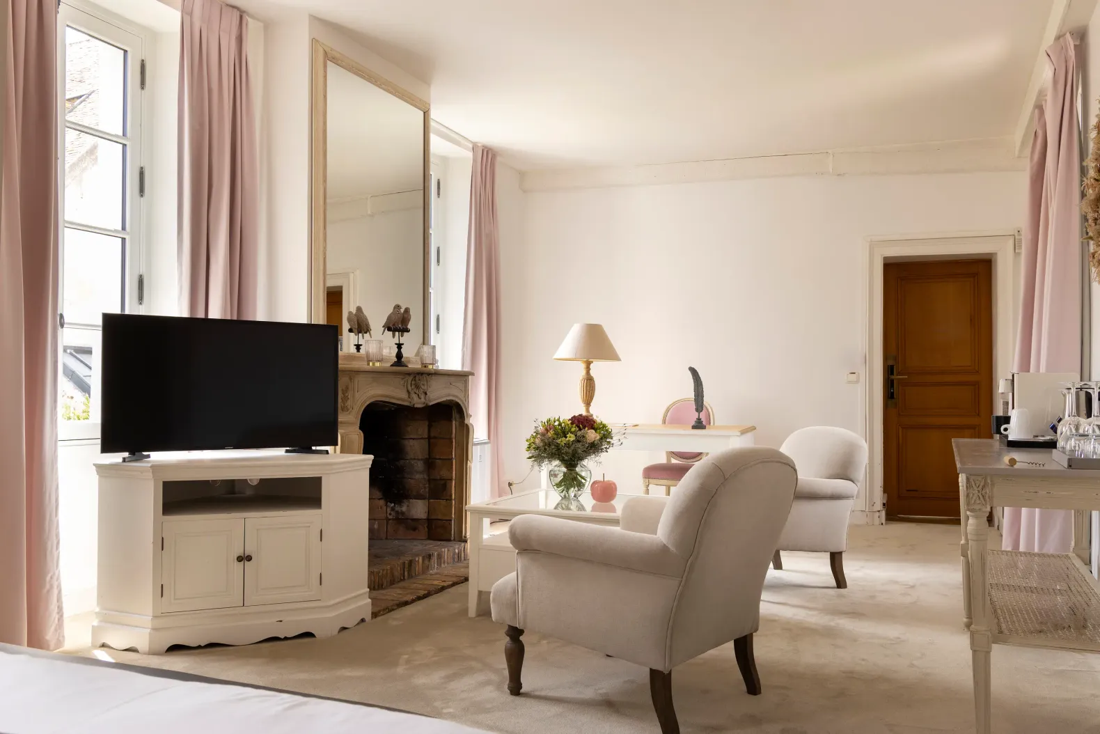 Salon avec télévision, cheminée, fauteuils, table basse et fenêtre aux rideaux roses