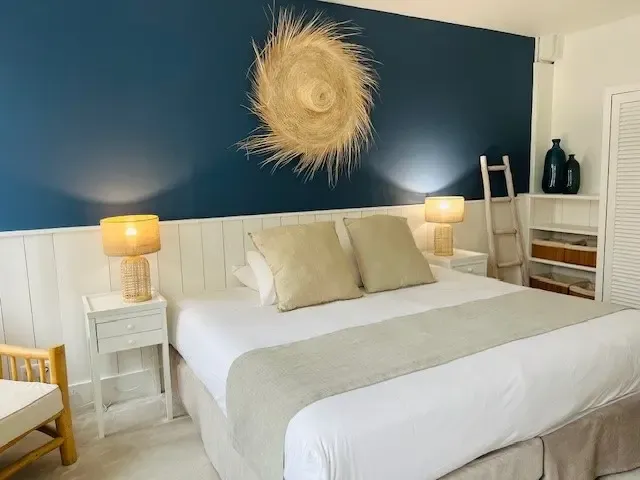 Chambre avec un lit double blanc, deux tables de chevet avec lampes, un mur bleu et une décoration murale en forme de spirale