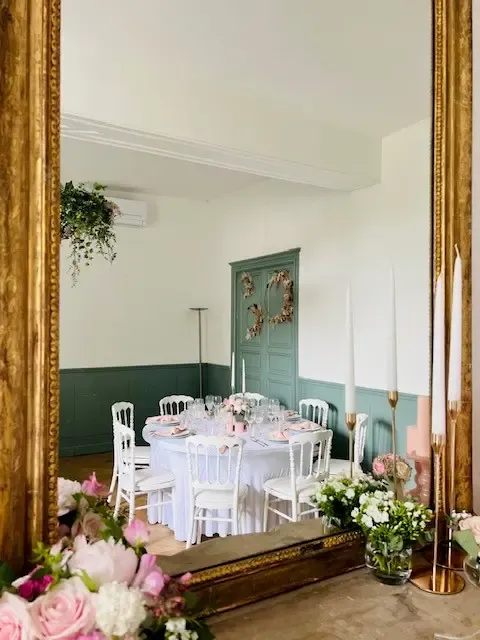 Une table ronde blanche avec des chaises assorties est décorée de fleurs et de bougies, entourée de miroirs dorés et de bouquets de roses