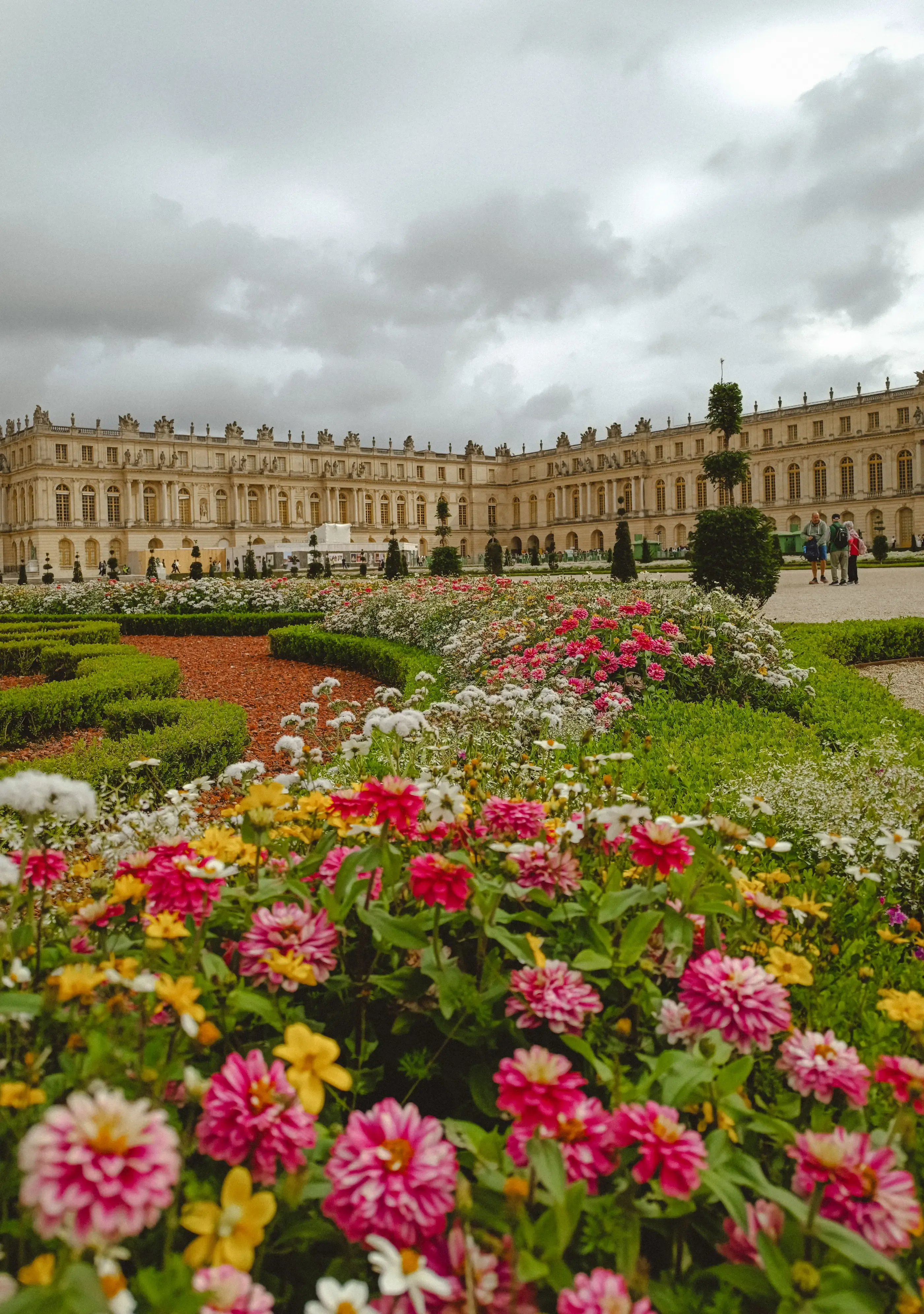 Un grand bâtiment classique avec des jardins fleuris à l'avant sous un ciel nuageux