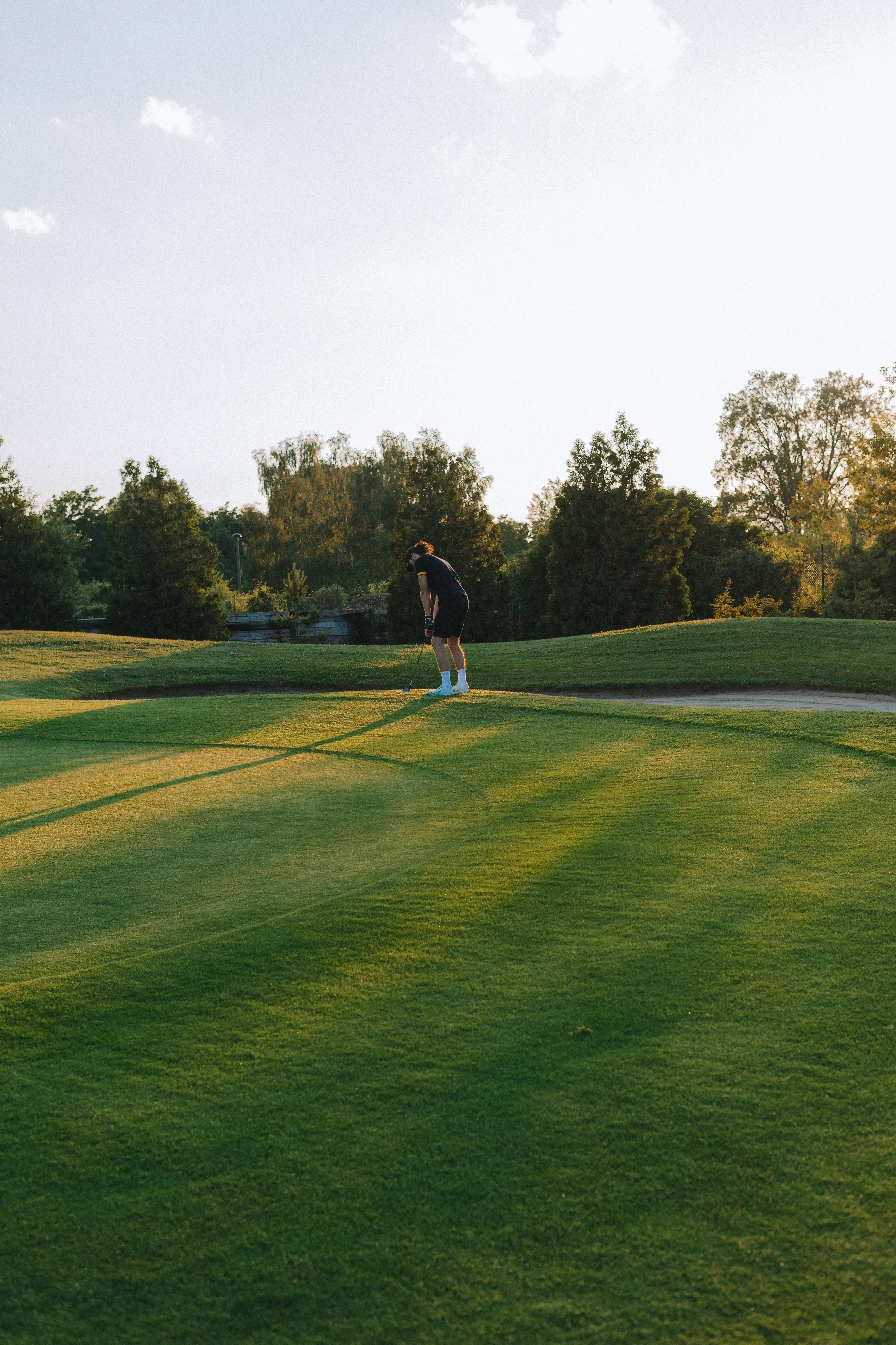 Un golfeur en tenue noire et blanche se prépare à frapper la balle sur un green entouré d'arbres