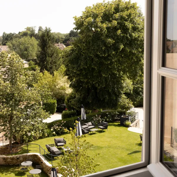 Vue d'un jardin avec des chaises longues, des tables et des arbres, vue depuis une fenêtre