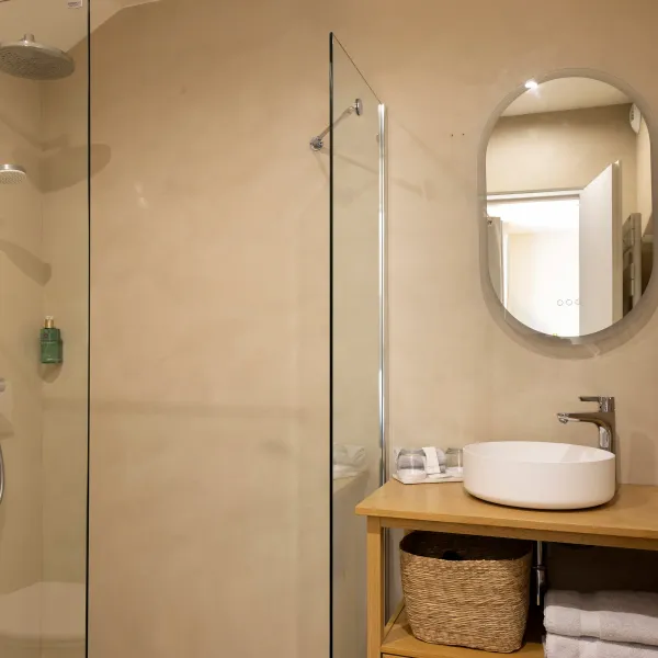 Salle de bain moderne avec douche à effet pluie, lavabo rond sur meuble en bois et miroir ovale