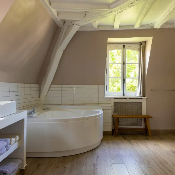 Salle de bain avec baignoire, double vasque, miroir et fenêtre ouverte sur un jardin