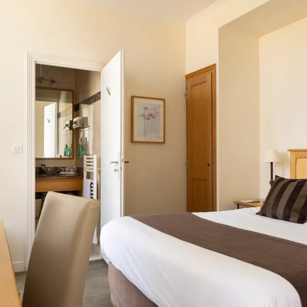 Chambre avec lit double, table de chevet, miroir et porte ouverte sur une salle de bain visible en arrière-plan