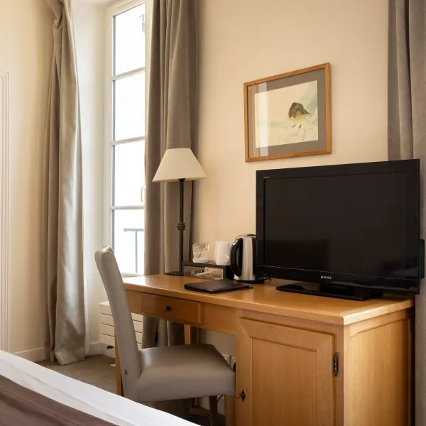 Bureau en bois avec télévision, lampe, bouilloire et chaise, près d'une fenêtre aux rideaux gris